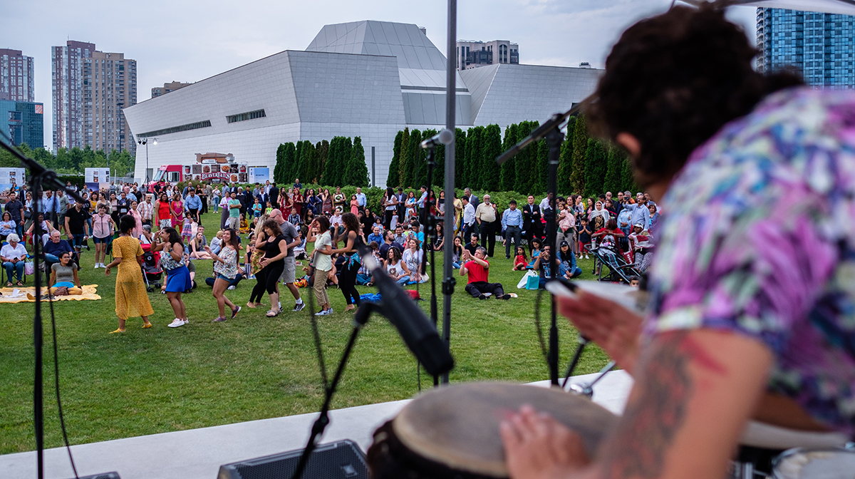 A group of people dancing outside in the background with a drummer in the foreground.